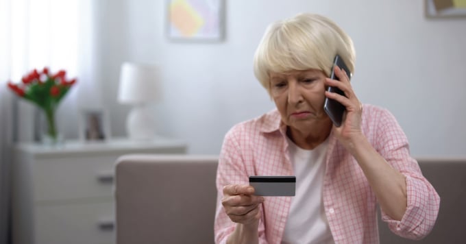 Elderly woman on the phone looking at her credit card.