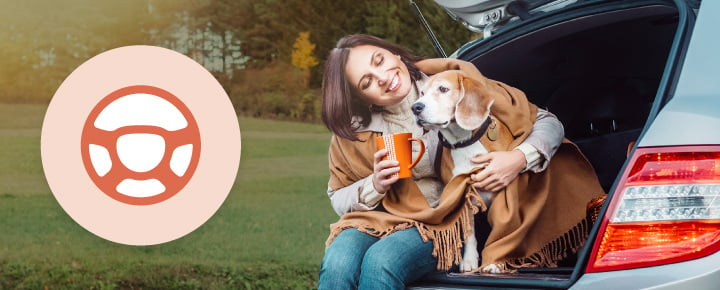 Woman with a beagle at a car trunk, wrapped in a blanket, holding an orange mug. Steering wheel icon is on the left.