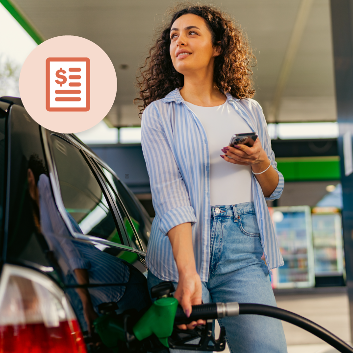 Curly-haired woman refueling a car at a gas station, holding a cellphone.